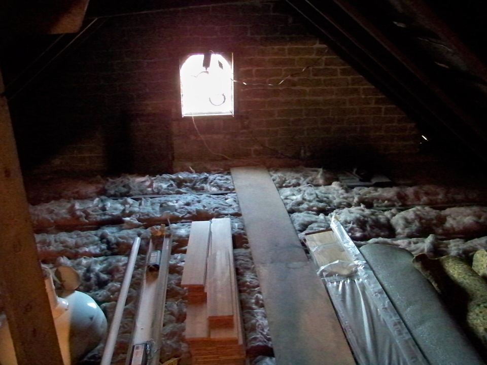 Loose-fill fiberglass insulation spread between attic floor joists beneath a gable window